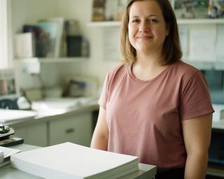 Klara Stein in einer Lokalredaktion neben einer gedruckten Ausgabe